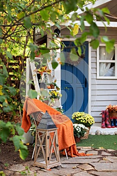 Cozy Autumn patio with chair, plaid, plants, wooden lantern, potted chrysanthemums. Halloween. Decorations in backyard for relax i