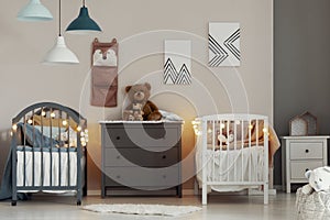 Cozy baby bedroom interior with white and grey cribs, commode and small nightstand table