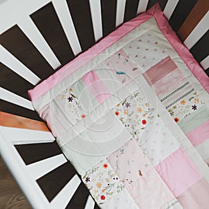 Cozy baby cot with pink patchwork blanket. Baby bedding. Baby crib, close up. Textile for children nursery. Nap and sleep time