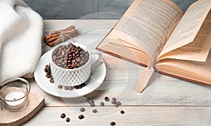 Cozy background with coffee beans in a Cup, a book, a sweater and candles.