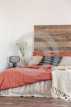 Cozy bedroom interior with white walls, wooden bedhead and red sheets. Real photo