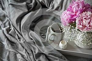 Cozy breakfast in bed, cup of coffee and milk on the grey fabric and pink pions, space for text. Breakfast in bed.