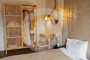 Cozy bright interior of a bedroom with a wooden wardrobe and clothes, a table, a chair and a bed