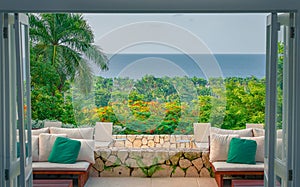 Cozy chairs inside of a beach house with open doors leading to palm trees and the ocean