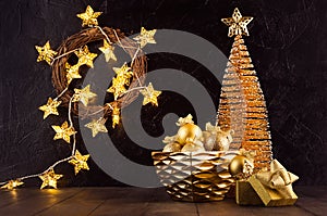 Cozy Christmas background with glowing golden stars lights, Christmas tree, wreath, balls, gift box, ribbons in modern black.