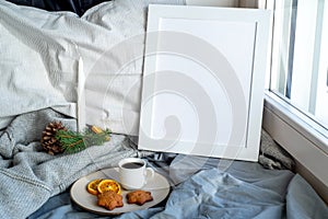Cozy Christmas breakfast still life scene near the window. Winter interior. Blank white picture frame mockup.Cup of coffee with