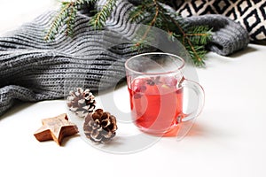Cozy Christmas morning breakfast scene. Steaming glass cup of hot fruit tea. Pine cones, wooden stars on white table