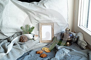 Cozy Christmas scene near the window. Winter interior. Blank wooden picture frame mockup. Wholemeal cookies, pillow, wool sweater,