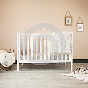 Cozy classic crib in a light baby room with toys on a soft carpet and a woven basket on the corner