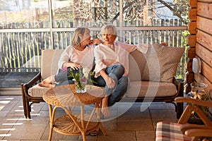 A cozy company of two 55-year-old girlfriends spending time at a nice conversation in wooden house with large windows