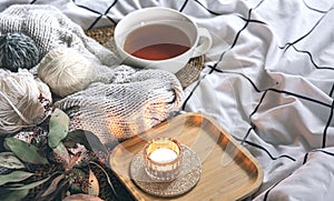 Cozy composition with a cup of tea, a candle and knitted elements on a blanket.