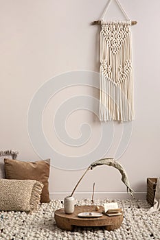 Cozy composition of meditation living room interior with beige carpet, pillows, macrame and personal accessories. Home decor.