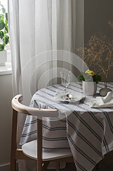 A cozy corner of the living room - a table set for dinner with a tablecloth and dishes, a chair