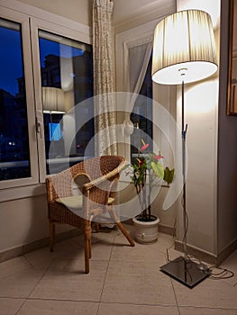 Cozy corner with wicker armchair, potted flowers and lighted lamp