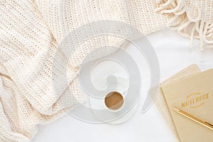 Cozy cream blanket on white bed with gold and natural notebooks, and espresso
