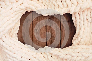 Cozy cream colored knitted thick wool blanket, overhead view frame on a rustic dark wood background