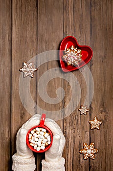 Cozy cup of hot chocolate in a red mug held by mittens with christmas cookies