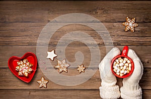 Cozy cup of hot chocolate in a red mug held by mittens with christmas cookies