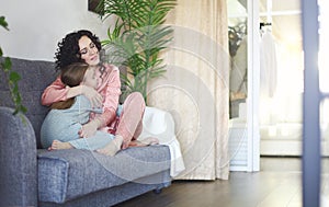 Cozy domestic photo of happy mother and daughter in pajamas relaxing on sofa in morning, young beautiful mom and little girl child