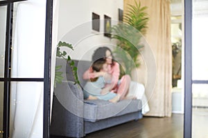 Cozy domestic photo of happy mother and daughter in pajamas relaxing on sofa in morning, young beautiful mom and little girl child