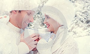 Cozy dressed couple drink hot tea on snow forest glade