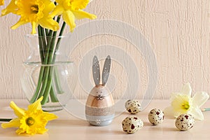 Cozy Easter background with decorative eggs, Easter bunny, daffodils on the table. Holiday greeting card. Selective