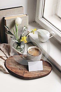 Cozy Easter spring still life. Business card mockup scene. Cup of coffee, books, wooden cutting board, milk pitcher and