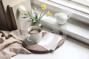 Cozy Easter spring still life. Greeting card mockup scene. Cup of coffee, books, wooden cutting board, milk pitcher and photo