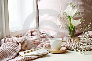 Cozy Easter, spring still life scene. Cup of coffee, opened notebook, pink knitted plaid on windowsill. Vintage feminine