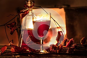 Cozy evening still life by . A glass of red wine, an old decanter, green leaves and dried flowers against a burning fire. Dark pho