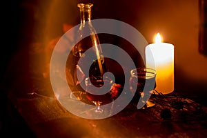 Cozy evening still life by . A glass of red wine, an old decanter, green leaves and dried flowers against a burning fire. Dark pho