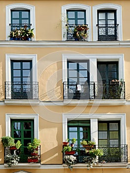 Cozy facade of warm colours with simple windows and balconies with flowers downtown Madrid, Spain. Vertical photo