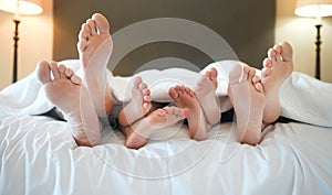 Cozy family lying in bed relaxing sleeping together. Feet and toes of parents and their tired little children sleeping