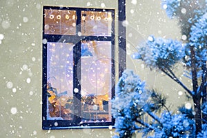 Cozy festive window of the house outside with the warm light of fairy lights garlands inside - celebrate Christmas and New Year in