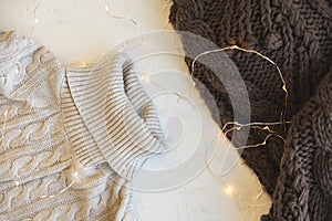 Cozy flat lay. Winter and autumn warm clothing: sweater, scarve and garland on white concrete textural background photo