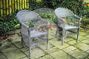 Cozy garden area for coffee and reading outside in the warm summer. Two grey woven lawn chairs on a stone patio outside