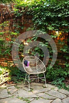 Cozy garden corner. Interior autumn patio. Wicker rattan chair outdoors in garden, on the background brick wall with curly wild gr