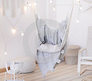 Cozy hammock chair in a bright room. Pastel colors. Gray bedspread. A garland of light bulbs