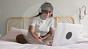 Cozy at home. African American young woman sitting on bed drinking hot coffee while watching show on laptop. Video.