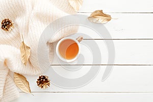 Cozy home desk table with knitted plaid, tea cup, fall leaves, cones on wooden white background. Top view, flat lay, copy space.