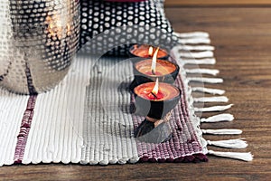 Cozy home interior decor, burning candles in coconut shell on a multi-colored rug with metal vase and decorative pillows