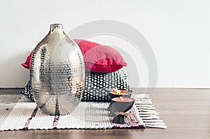 Cozy home interior decor, burning candles in coconut shell on a multi-colored rug with metal vase and decorative pillows