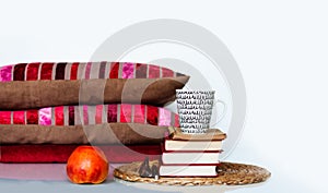 Cozy home interior decor: cup of coffee, apple, stack of books, pillows and plaid on a white table. Distance home education.