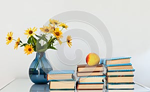 Cozy home interior decor: stack of books, peach and vase with yellow flowers on a table. Distance home education.Quarantine