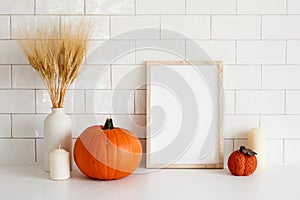 Cozy home interior with frame mockup, autumn fall decorations, pumpkins, vase of wheat, candle. Scandi, minimal style. Poster