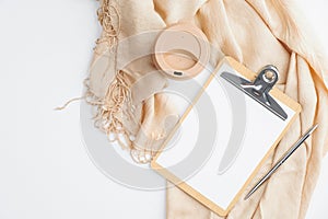 Cozy home office desk with beige blanket, cup of coffee, clipboard with empty paper note on white background. Flat lay, top view.