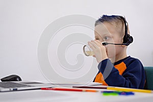 Cozy home schooling. Cute little  schoolboy typing on laptop, studying remotely at home and drinking orange juice