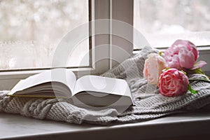 Cozy home still life: spring flowers and opened book with warm plaid on windowsill. Springtime concept, free copy space