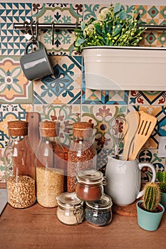 Cozy home style modern kitchen with colorful patchwork tiles, spice jars, glass jars with cereals and other kitchen accessories