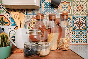 Cozy home style modern kitchen with colorful patchwork tiles, spice jars, glass jars with cereals and other kitchen accessories